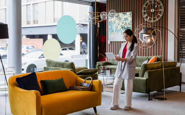 A woman standing in the furniture store, taking a picture of a sofa with a digital tablet.