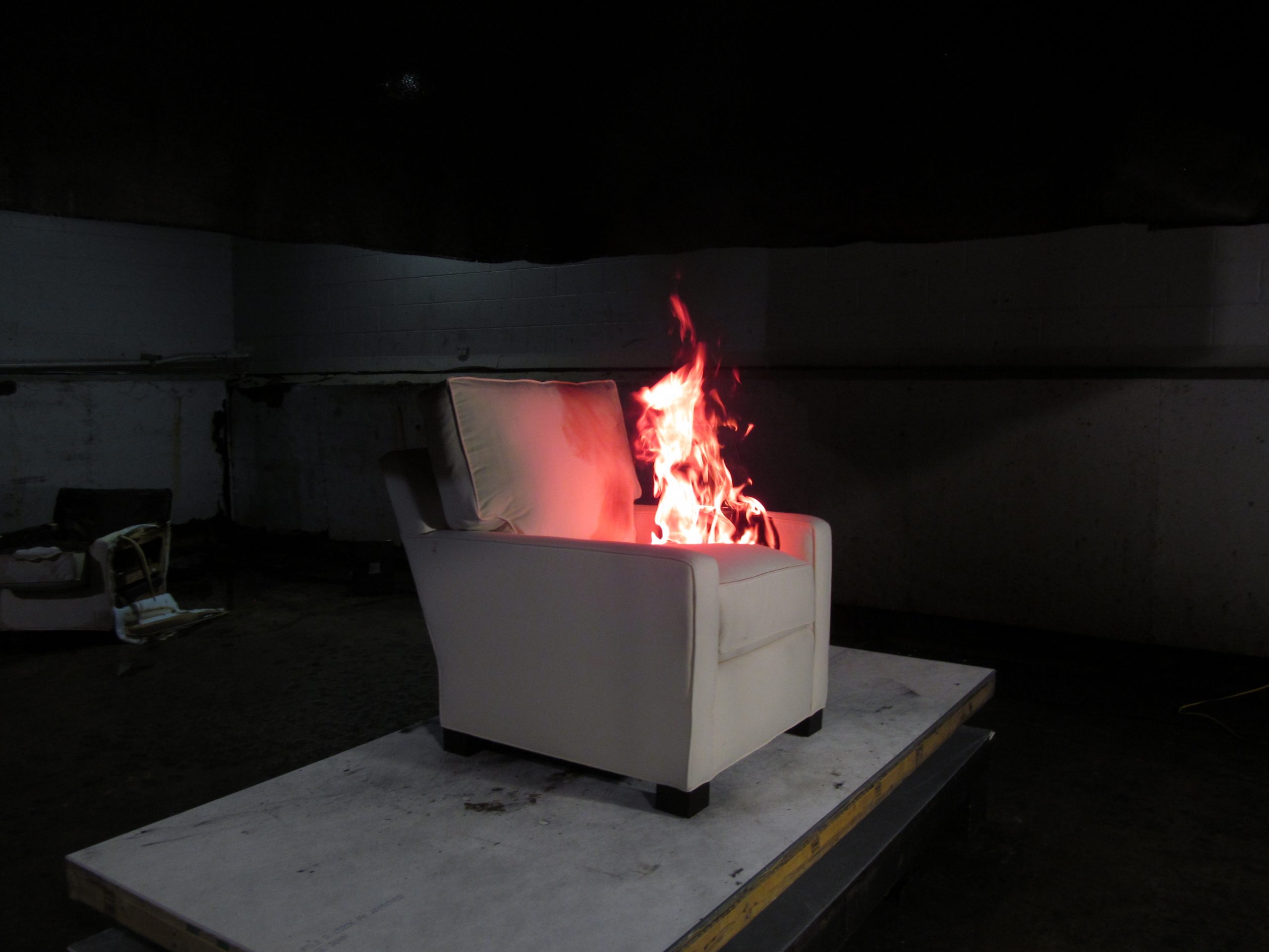 White lounge chair on industrial platform. Red flames rise from the seat cushion.