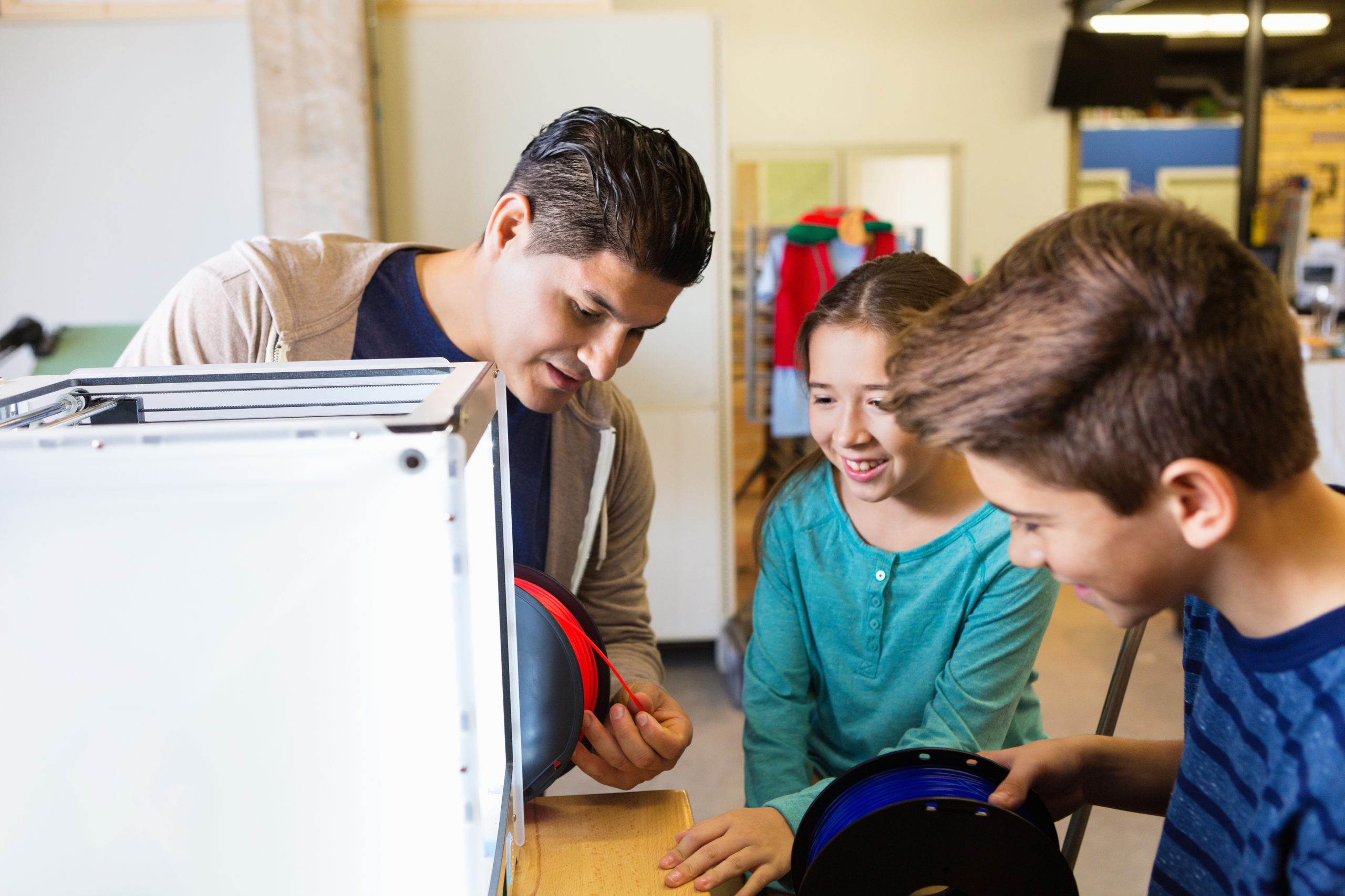 Children and an adult 3D printing with blue and red material.